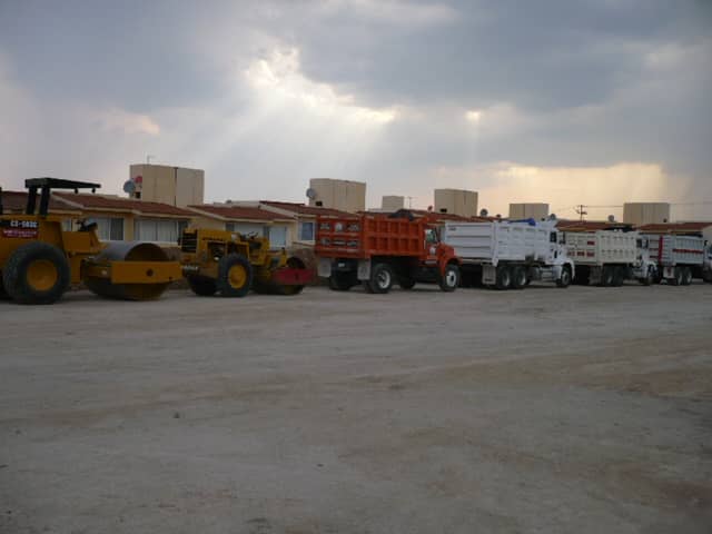 Flota de vibrocompactadores y camiones de volteo al atardecer